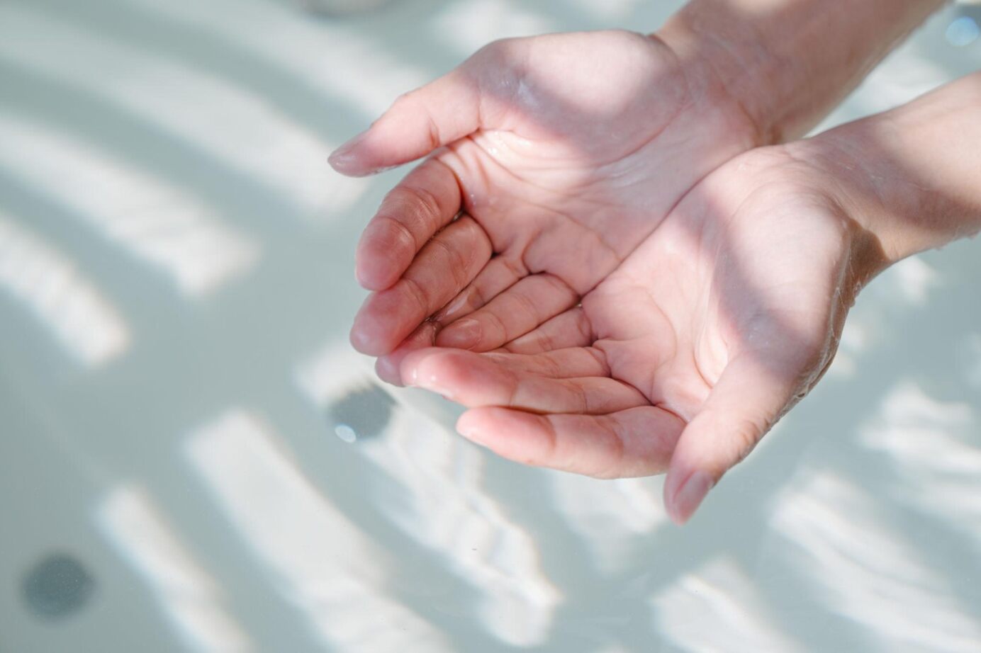 Hände halten Wasser in sanften Lichtreflexionen.
