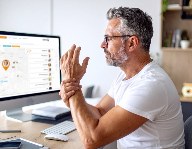 Mann mit Handgelenkschmerzen am Computerarbeitsplatz